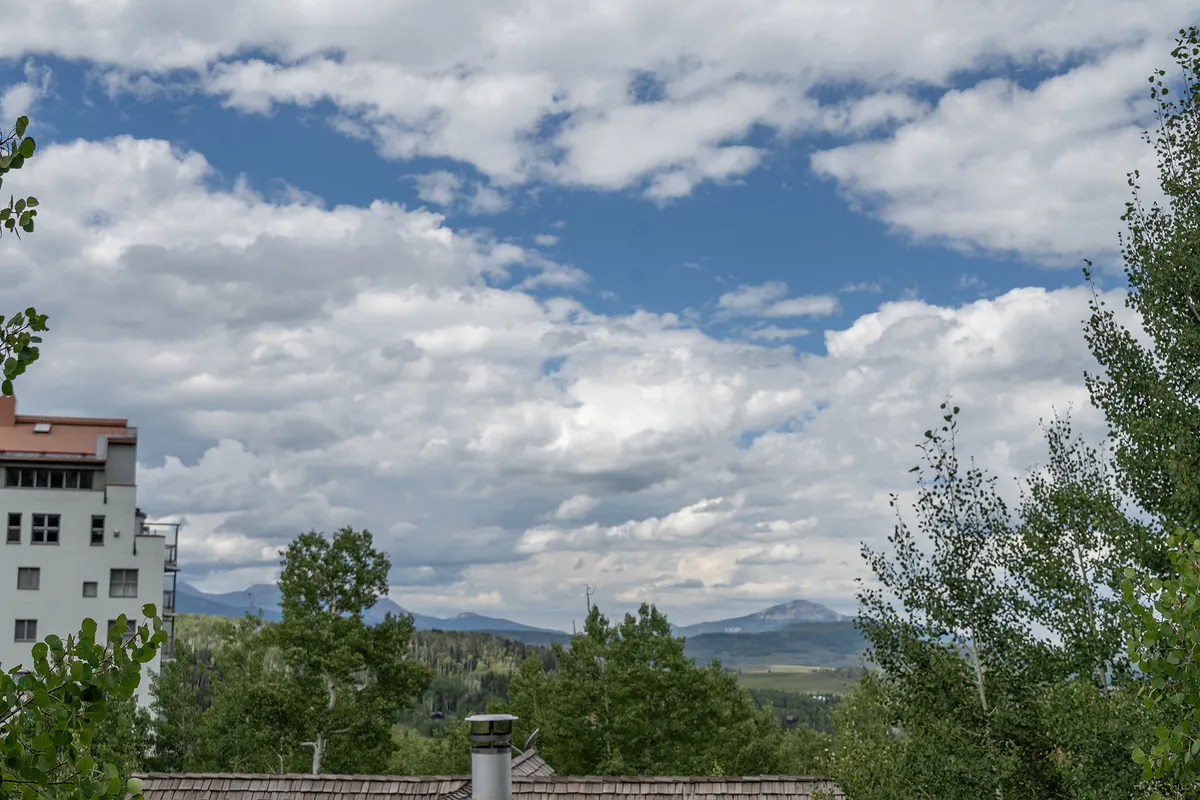 This scenic view features majestic mountains, a cloudy sky, and lush green trees, creating a tranquil mountain backdrop. The natural landscape conveys the serenity and beauty of Telluride’s outdoor environment.