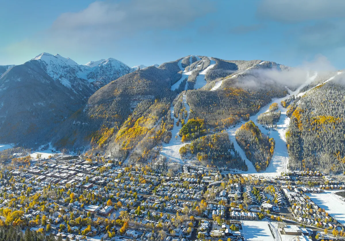 This vibrant exterior image captures snow-covered mountains, winding ski slopes, and colorful autumn trees with a picturesque town nestled below. The scenery highlights both the thrill of winter activities and the beauty of the landscape, suggesting year-round outdoor adventure.