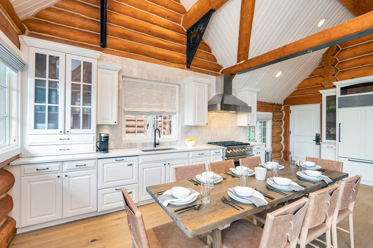 An inviting dining area highlighted by a wooden table set for a meal, with modern kitchen appliances in the background. Rustic log walls and wooden beams add warmth and character, while the setup is ideal for family meals or entertaining guests after a day of mountain adventures.
