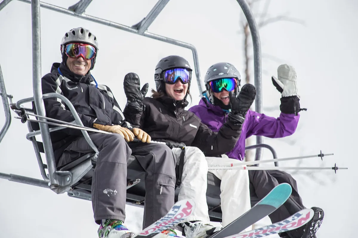 A lively winter scene with three skiers riding a lift, surrounded by snow-draped peaks. The image conveys the excitement and camaraderie of mountain sports, highlighting the proximity to world-class skiing.