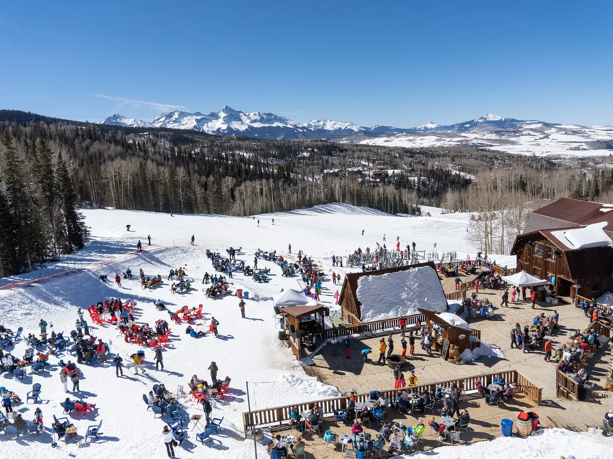 A lively exterior scene with people skiing on snow-covered slopes, a nearby wooden lodge, and an outdoor seating area with panoramic views of the surrounding mountains. The joyful mood reflects the excitement of ski season and resort camaraderie.
