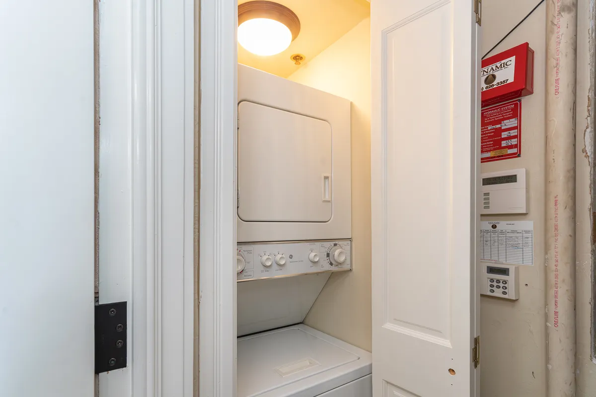 A bright, efficient laundry area featuring a stacked washer and dryer, situated in a practical space with a door frame and overhead lighting. The setup is clean and modern, emphasizing convenience for families needing to keep up with laundry on the go.